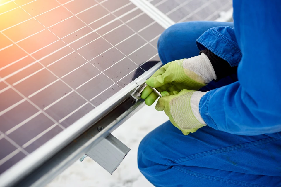 Technicien en combinaison bleue installant des panneaux solaires photovoltaïques sur toiture