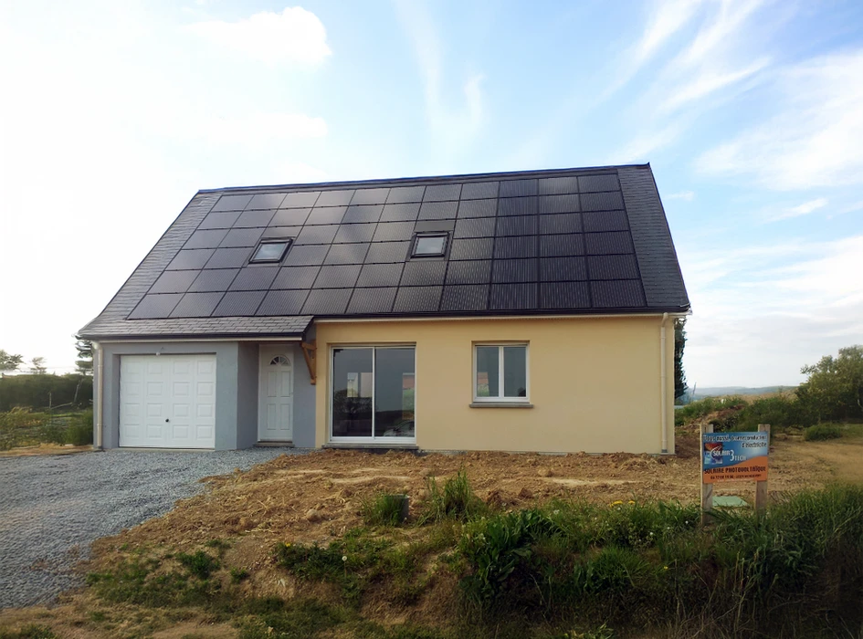 Maison individuelle moderne en construction avec toiture entièrement couverte de panneaux photovoltaïques noirs, garage attenant, façade beige et grise