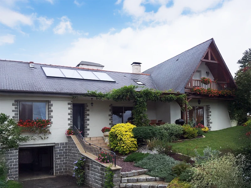 Maison individuelle avec façade blanche, toiture en ardoise équipée de panneaux solaires thermiques et photovoltaïques