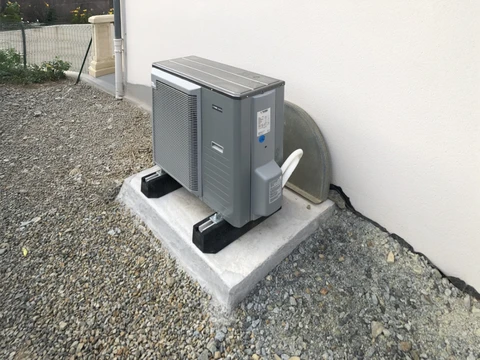 Extérieur résidentiel avec unité de climatisation installée sur dalle béton contre mur blanc