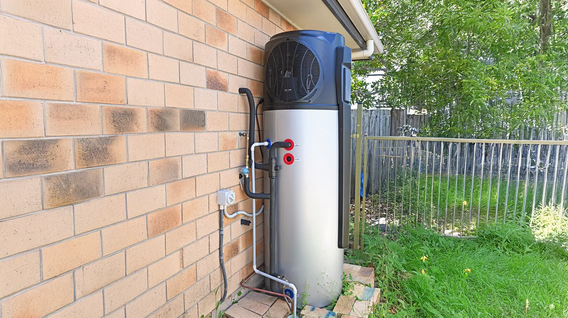 Une main masculine ajuste le thermostat d'un chauffe-eau électrique blanc installé sur un mur