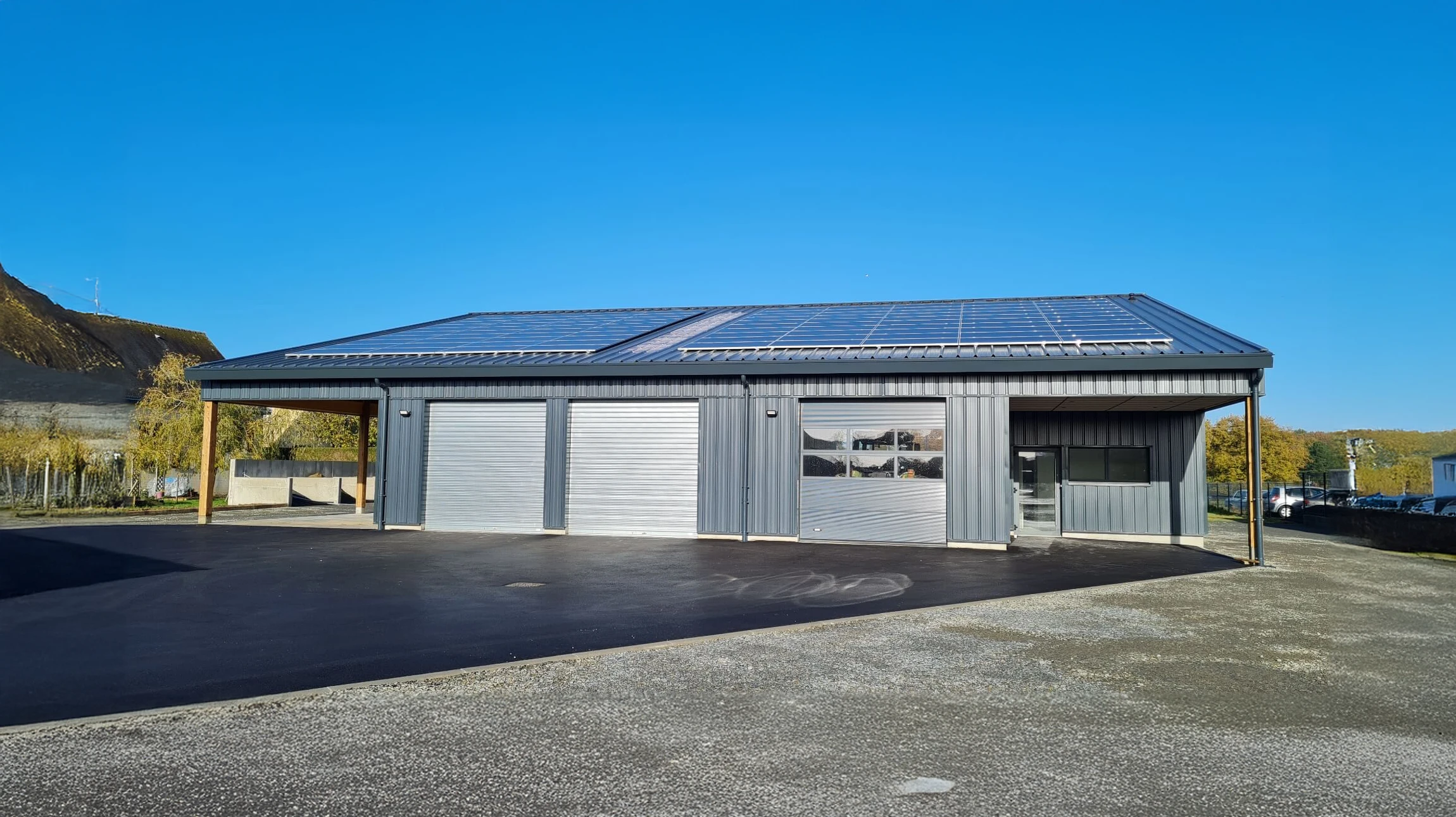 Maison r&eacute;sidentielle en briques avec toiture &eacute;quip&eacute;e de panneaux solaires photovolta&iuml;ques noirs, deux lucarnes &agrave; fen&ecirc;tres blanches, ciel bleu nuageux